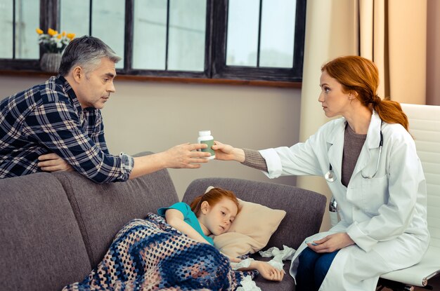 Prescrição de médicos. Homem bonito e bonito olhando para o médico enquanto toma um frasco de comprimidos