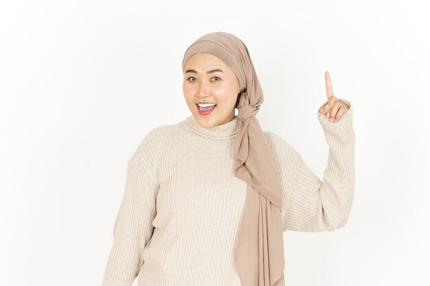 Presentación y apuntando hacia arriba de la hermosa mujer asiática vistiendo Hijab aislado sobre fondo blanco.
