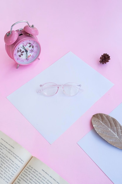 Presentación del producto de los anteojos Minimalist Concept Idea libro reloj hojas secas sobre fondo de papel rosa