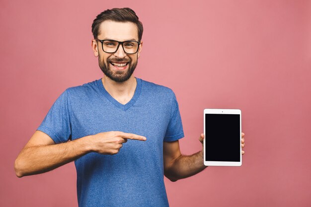 Presentacion de producto. Promoción. Hombre joven que se sostiene en tableta de las manos con la pantalla en blanco, cierre. Aislado sobre fondo rosa