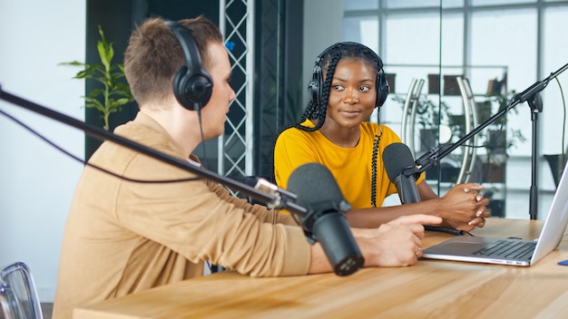 Un presentador masculino se comunica con un invitado afroamericano durante una transmisión de radio en una mesa en un estudio de grabación transmite una entrevista de radio en vivo con Spbd