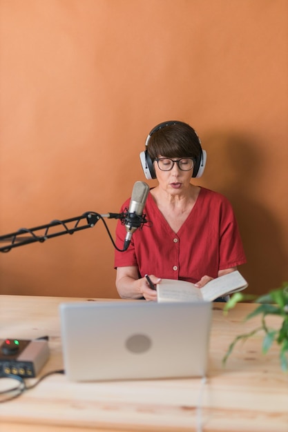 Presentadora de radio de mediana edad hablando en el micrófono y leyendo onli de transmisión de radio de noticias