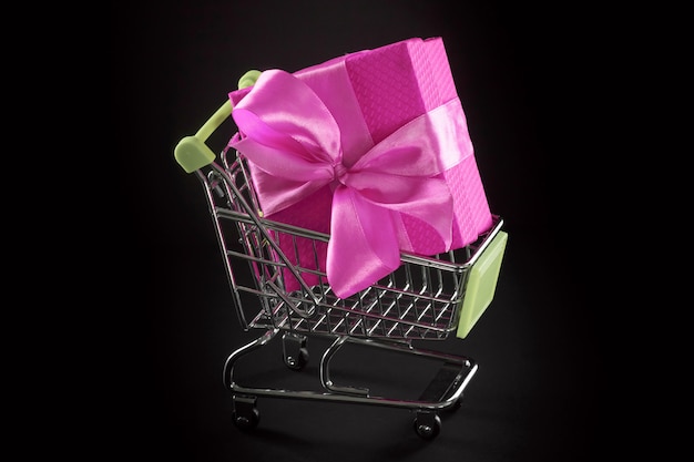 Presente caixa de presente em embalagens festivas com laço de cetim no carrinho de compras.