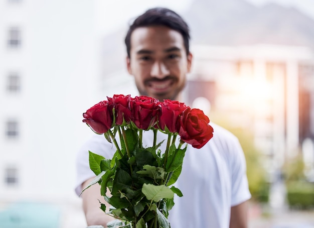 Presente de amor e retrato de homem feliz com rosas para romance de encontro e dia dos namorados Sorria esperança romântica e pessoa dando buquê de flores em proposta de cidade ou noivado em fundo desfocado