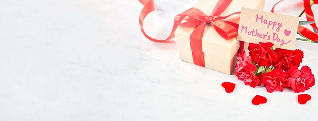 Presente de dia das mães, buquê de flor cravo vermelho com presente kraft embrulhado amarrado com fita isolada na mesa de mármore branco, close-up.