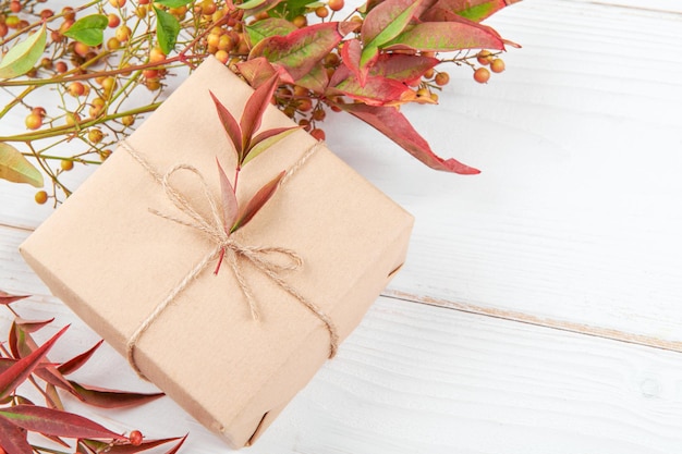 Presente de férias criativo de outono. caixa de presente de papel artesanal com folhas de folhagem vermelha e laranja, sobre fundo branco de madeira. dia de ação de graças, fundo de outono. copiar espaço