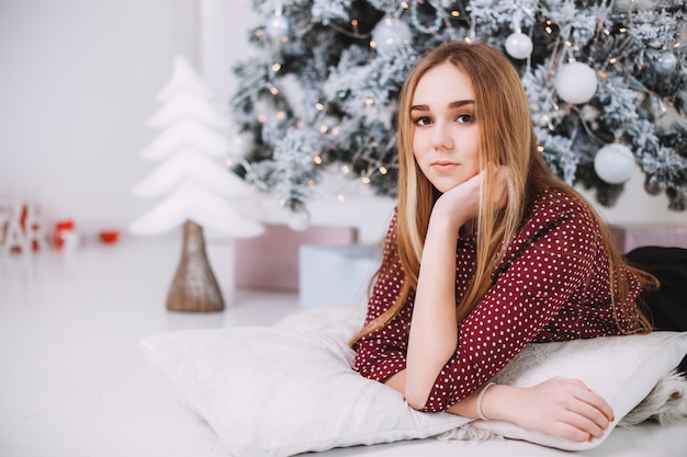 Presente de Natal. Celebração de Ano Novo. Lindo feriado decorado quarto com árvore de Natal com presentes debaixo dele. Ano novo e conceitos de Natal. Linda garota sentada perto de árvore do ano novo.