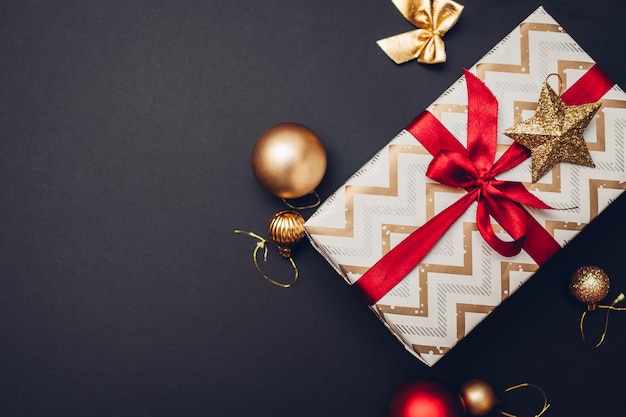 Presente de Natal e ano novo embrulhado em papel natalino e decorado com fita vermelha e enfeites dourados, brinquedos, bolas em fundo preto. Espaço