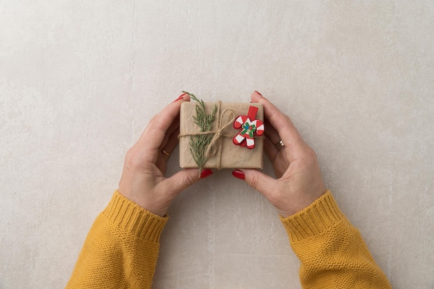 Presente de natal em mãos femininas em uma jaqueta amarela, vista de cima, fundo claro de concreto