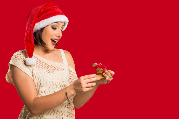 Foto presente de natal - mulher abrindo presente surpresa e feliz, bela jovem sorridente com chapéu de papai noel