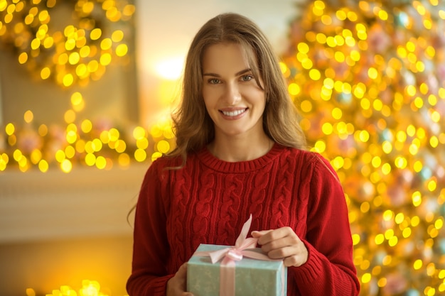 Presente de Natal. Mulher jovem de cabelos escuros em pé com um presente nas mãos