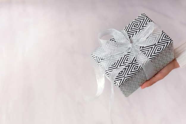 Presente de Natal na mão. Uma garota de suéter branco segura um presente embrulhado em papel preto e branco