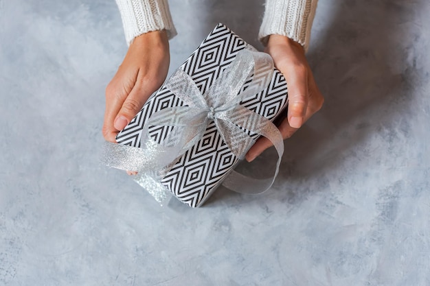 Presente de Natal na mão Uma garota em um suéter branco de inverno segura uma caixa embrulhada em papel preto e branco