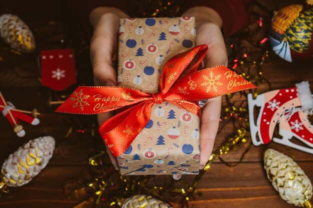 Presente de Natal nas mãos da mulher na mesa de madeira Mãos femininas segurando um presente de ano novo. Decoração de ano novo