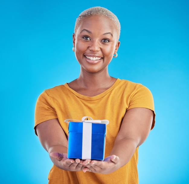 Presente de retrato e mulher negra feliz com oferta em estúdio isolado em um fundo azul Face dando e pessoa com caixa de presente para celebração de festa ou pacote de aniversário para oferta de doação