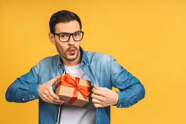 Presente maravilhoso Foto adorável de homem barbudo atraente com lindo sorriso segurando caixa de presente de aniversário isolada sobre fundo amarelo