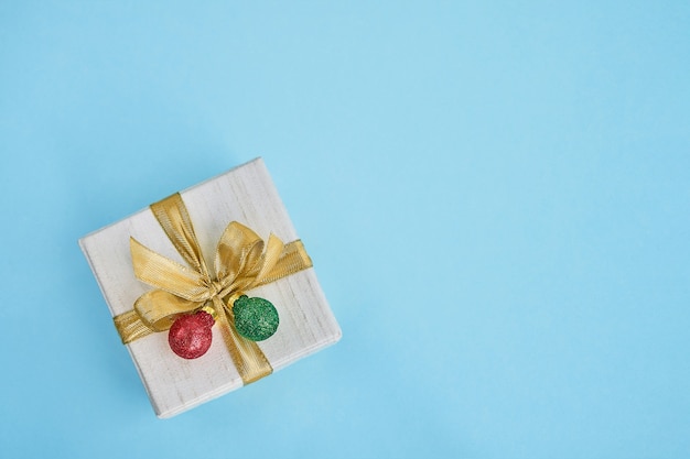 Foto presente ou caixa de presente decorada com fita dourada e bolas de natal em fundo azul. vista superior, copie o espaço. fundo de natal. cartão de felicitações.