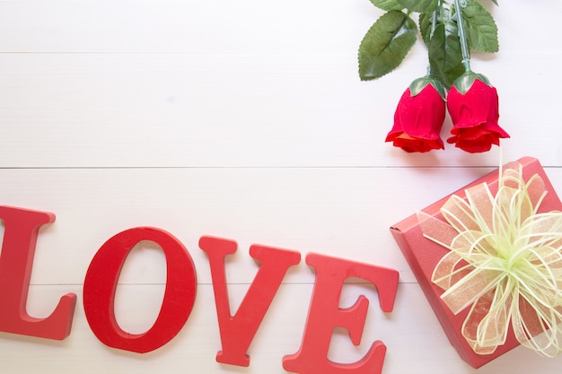Presente presente com flor rosa vermelha e caixa de presente com fita de arco na mesa de madeira