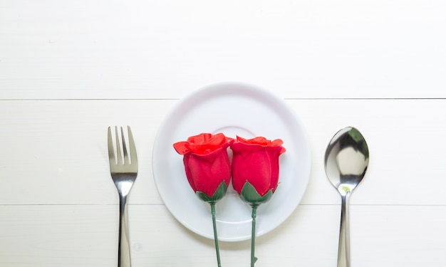 Presente presente com flor rosa vermelha e prato e colher e garfo na mesa de madeira