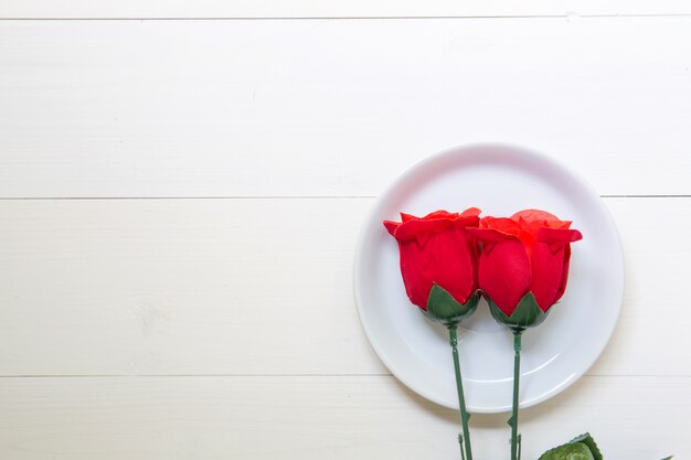Presente presente com flor rosa vermelha e prato na mesa de madeira