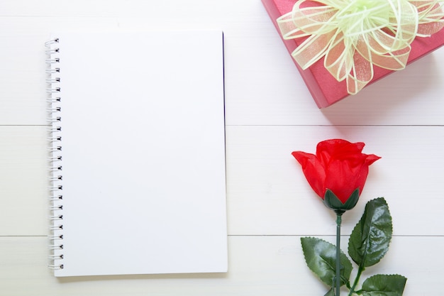 Presente el regalo con la flor de la rosa roja y el cuaderno con el espacio de la copia en la tabla de madera