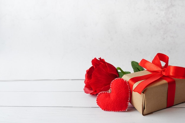 Presente vermelho ou caixa de presente com fita de arco, flor rosa e coração em fundo branco de madeira, cartão para dia dos namorados.