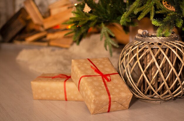 Presentes de ano novo e cesta de vime sob linda árvore de natal com lareira lareira e fundo da parede de tijolos cinza.