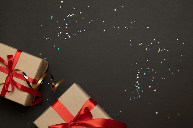 Presentes de artesanato de Natal com fitas vermelhas e confetes de ouro sobre um fundo de contraste escuro