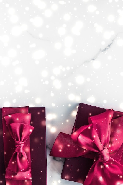 Presentes de férias de inverno com arco de seda cereja e neve brilhante sobre fundo de mármore congelado Presentes de Natal surpresa