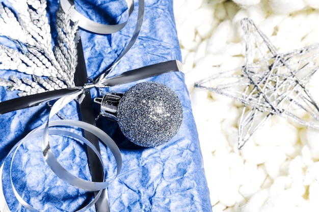 Presentes de Natal com caixa de presente na cor azul prata decorada com pinhas e galhos em fundo branco, preparação para festas. Presentes de Natal e Reveillon. Feito à mão. Foco seletivo.