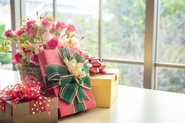 Presentes de Natal com vaso rosa e chapéu de Papai Noel no interior da mesa de madeira da sala vista através da janela