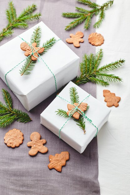 Presentes de Natal embrulhados em papel branco e decorados com raminhos de abeto e biscoitos de gengibre em um fundo de tecido