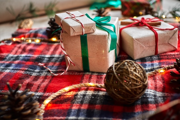 Presentes de Natal no fundo de uma manta xadrez de lã vermelha com guirlandas de cones e ramos de abeto