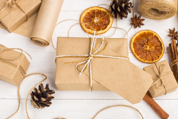 Presentes de papel ofício, laranja seca, canela, pinhas, anis em uma mesa branca