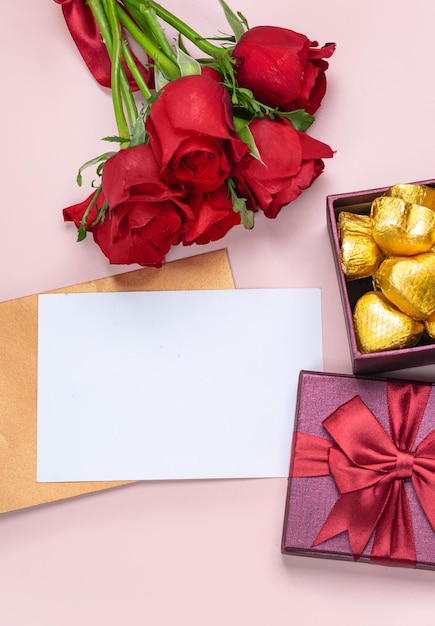 Presentes e rosas vermelhas em um fundo rosa com cartão branco em branco Conceito dos namorados Copie o espaço