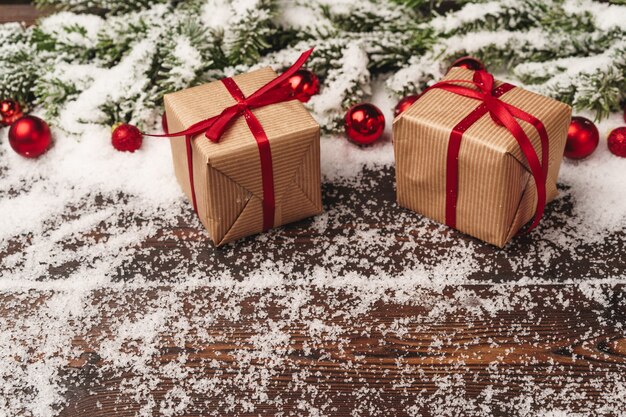 Presentes em fundo de madeira com galhos de pinheiros e enfeites vermelhos polvilhados com neve