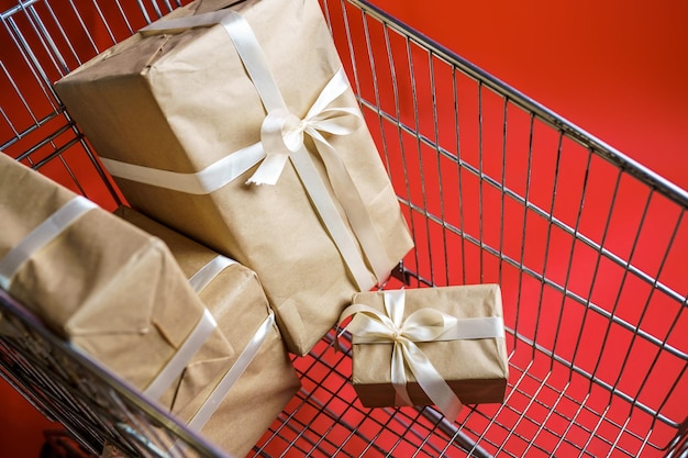 Presentes em papel artesanal com fita branca em um carrinho de supermercado sobre um fundo vermelho