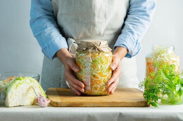 Preservação da fermentação Chucrute em frascos de vidro nas mãos de uma mulher fundo natural Conceito de comida enlatada