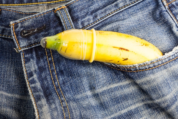 Preservativo e banana prontos para sexo seguro em fundo de calça jeans.