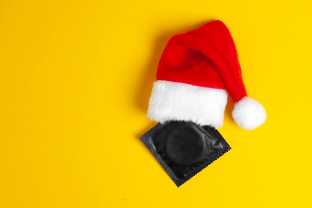 Foto preservativo preto com chapéu de ano novo em fundo amarelo, um presente sexy para o ano novo