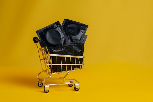 Foto preservativos pretos estão em um carrinho de compras em um fundo amarelo comprando conceito de desconto de contraceptivos