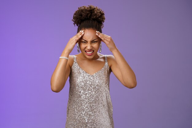 Presionada intensamente preocupada mujer afroamericana en vestido plateado brillante haciendo muecas de dolor ...