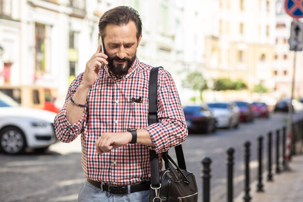 Pressão do tempo. Homem simpático e bonito falando ao telefone enquanto verifica o tempo ao ar livre