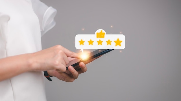 Pressionando a mão na tela do smartphone com o ícone de feedback de classificação de cinco estrelas em ouro e pressione o nível de classificação excelente para dar o melhor ponto de pontuação para revisar o conceito de negócios de serviços