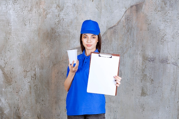 Prestadora de serviço feminina de uniforme azul segurando um copo descartável branco e pedindo assinatura