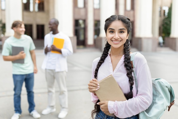 Préstamos para el retrato del concepto de educación de una feliz estudiante india posando al aire libre en el campus con