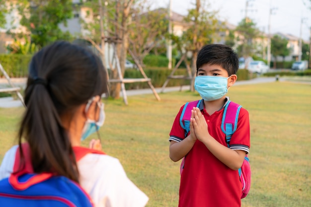 Prestar respeto es un saludo nuevo y novedoso para evitar la propagación del coronavirus. Dos niños asiáticos preescolares amigos se encuentran en el parque escolar con las manos desnudas.