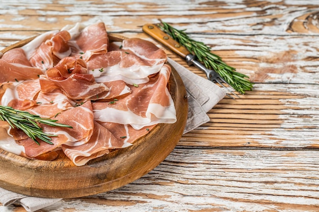 Presunto de parma curado a seco ou prosciutto crudo em uma placa de madeira com alecrim. fundo de madeira branco. vista do topo. copie o espaço.