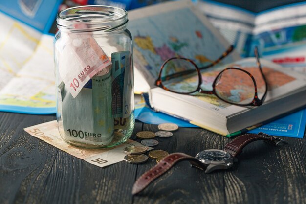 Presupuesto de viaje: ahorro de dinero en vacaciones en un frasco de vidrio en el mapa mundial