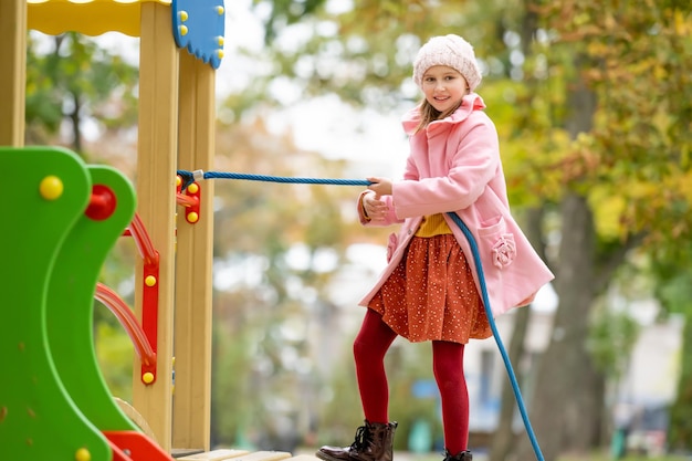 Preteen Mädchen Kind Klettern auf Spielplatz im Herbstpark Blick in die Kamera und lächelnde glückliche weibliche...